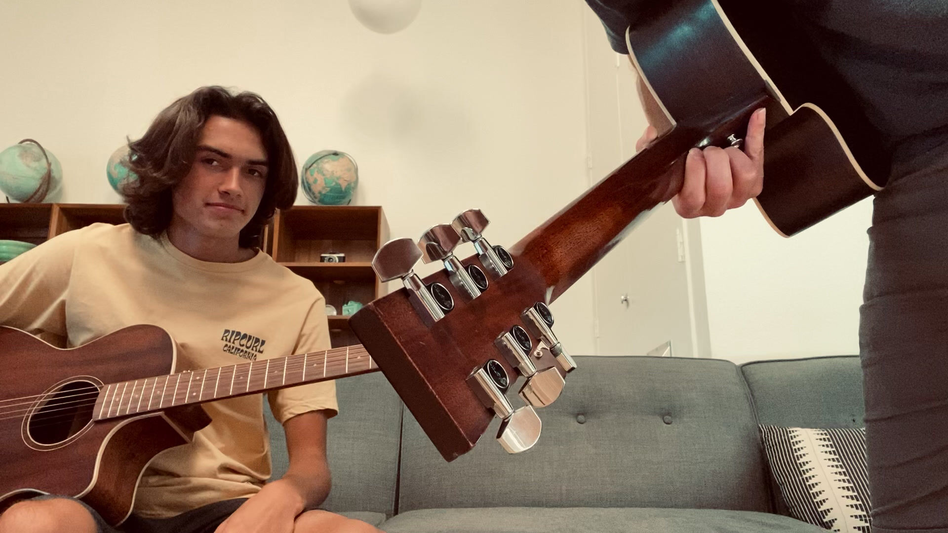 Teen student practicing acoustic guitar with the teacher's guitar in the foreground